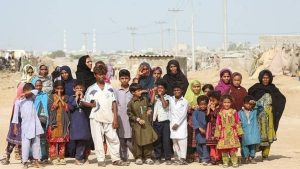 Baluch women and children stand in a dusty village on the outskirts of Zahedan