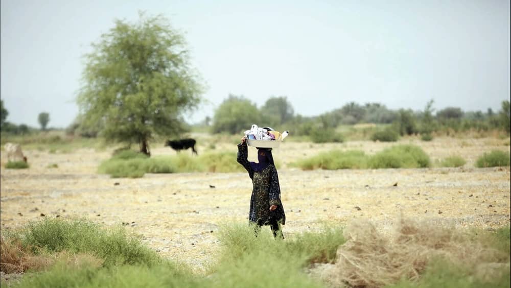 An Iranian woman walks across a dry plain carrying household supplies