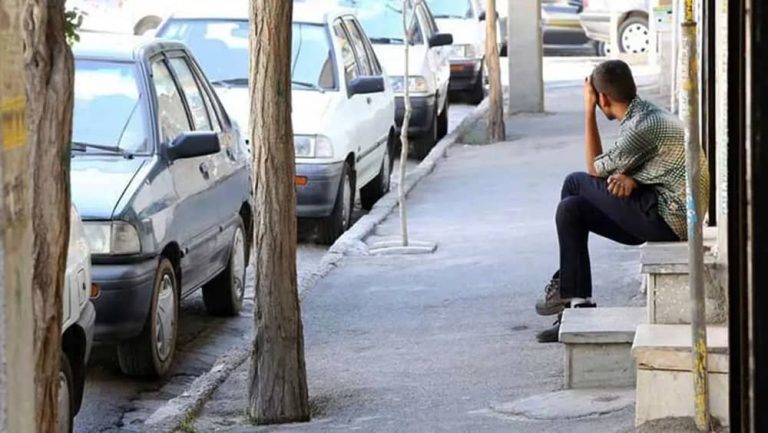 Young man sits on a sidewalk in an Iranian city amid worsening economic conditions and rising unemployment