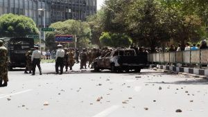 Security forces stand near a burnt-out vehicle amidst a street littered with debris following clashes in Tehran during the July 1999 student uprising