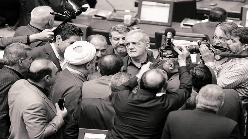 Hardline cleric and MP Hamid Rasaee (white turban, left of center) argues with the Iranian regime's president Masoud Pezeshkian as journalists and fellow lawmakers crowd around them in Parliament