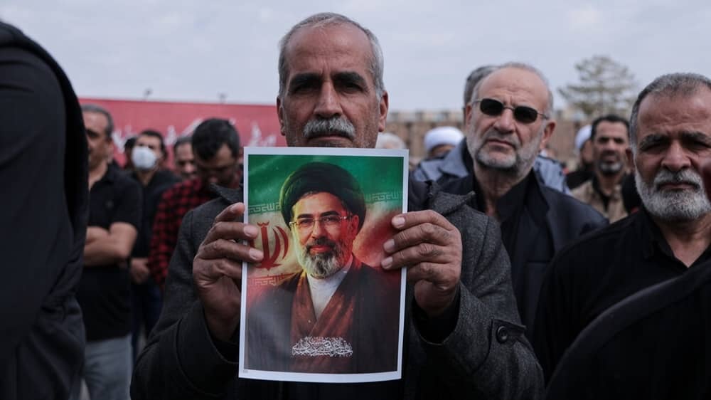 A regime-aligned mourner holds a portrait of Mojtaba Khamenei during a state-staged gathering in Iran