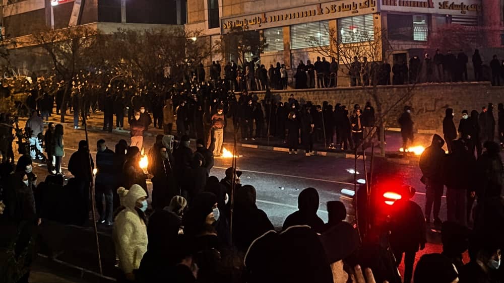 Protestors gather on a street in the Jannatabad neighborhood of Tehran at night, lighting small fires on the pavement—January 8, 2026